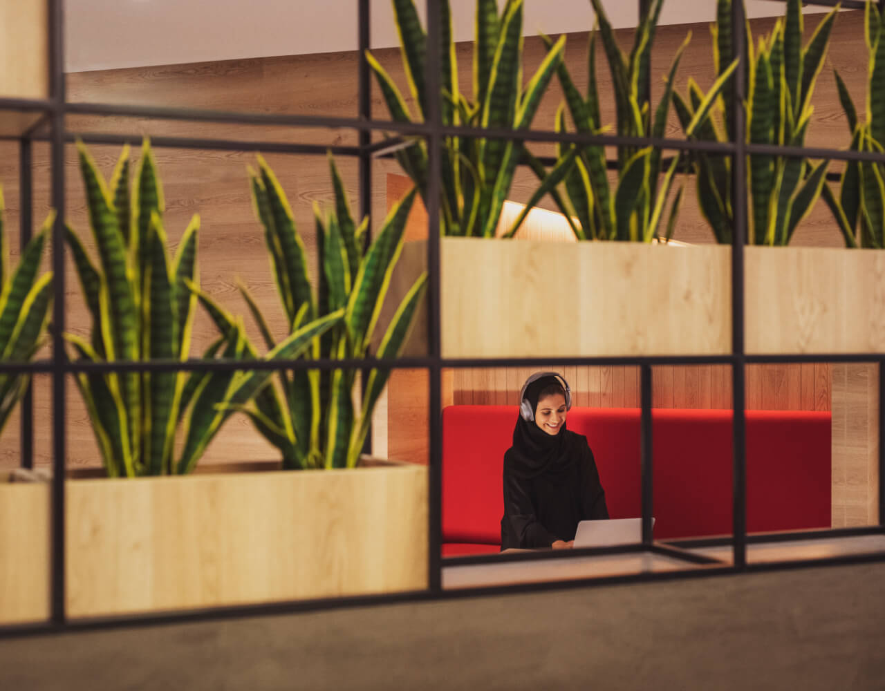  A happy woman with headphones working on her laptop at one of Dubai Outsource City's commercial office spaces for rent
